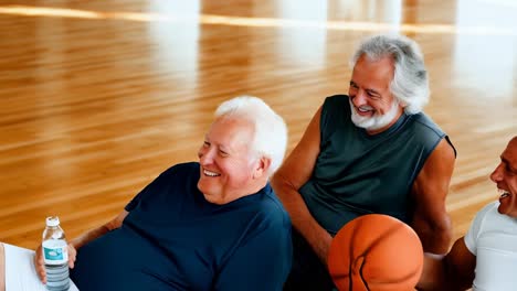 a group of men are sitting on a bench in a gym, laughing