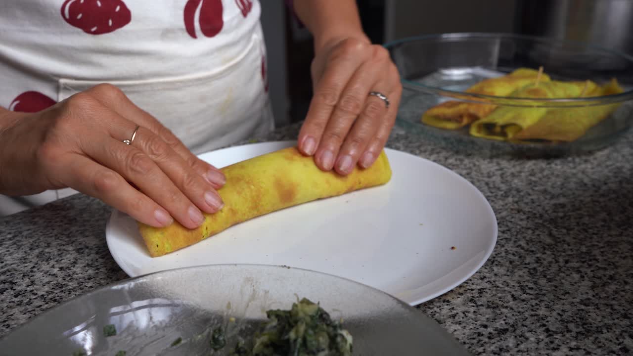 mujer esparciendo canelones rellenos sobre lámina de pasta con jamón
