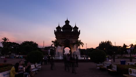 Patuxai-monument-lighting-up-at-sunset,-Vientiane-with-people-in-foreground