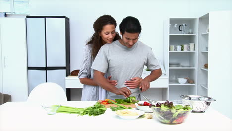 mujer comiendo mientras su marido está cocinando verduras
