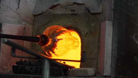 shaping a blown glass vase in a kiln at a demonstration in murano.