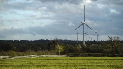 Windmills-in-a-forested-landscape-wind-farm-on-a-cloudy-day-with-field-in-foreground-4k