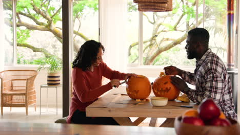 halloween time, multiracial couple carving pumpkins at home, enjoying festive autumn activity