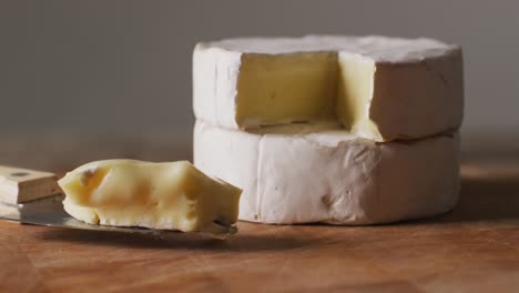 Video-close-up-of-soft-cheeses-and-knife-on-wooden-chopping-board,-with-copy-space