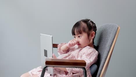 Asian-child-with-fringe-in-hair-sitting-on-chair-laughing-while-using-digital-tablet