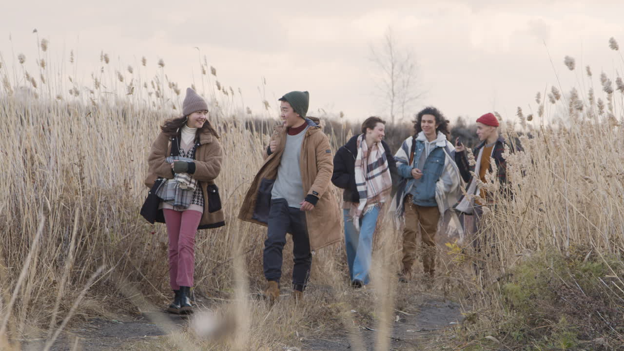 흐린 날 밀밭을 걷고 있는 겨울 옷을 입은 10대 소년 소녀들의 전면 모습