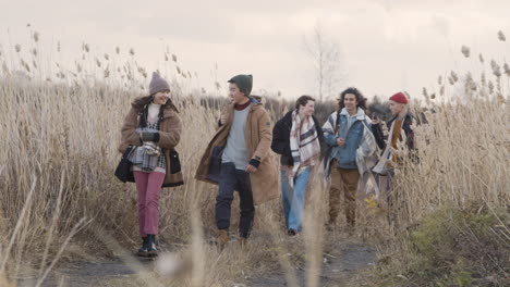 front view of a group of teenage boys and girls wearing winter clothes walking in a wheat field on a cloudy day