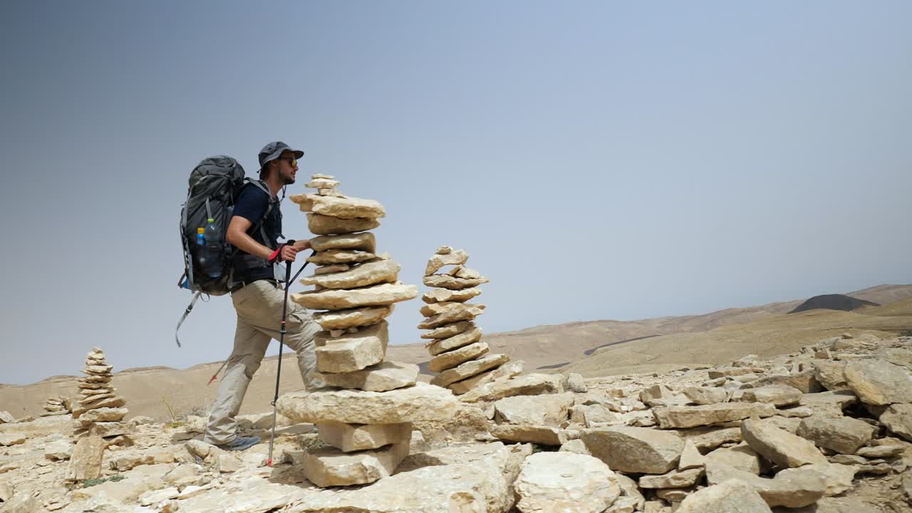 vista estática de un joven mochilero feliz caminando en el pico de la montaña entre piedras paradas una encima de la otra