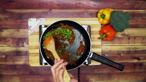 una vista superior de mezclar los ingredientes en una sartén, colocados en una estufa, dos grandes pimientos amarillos y rojos y un brócoli verde sobre la mesa