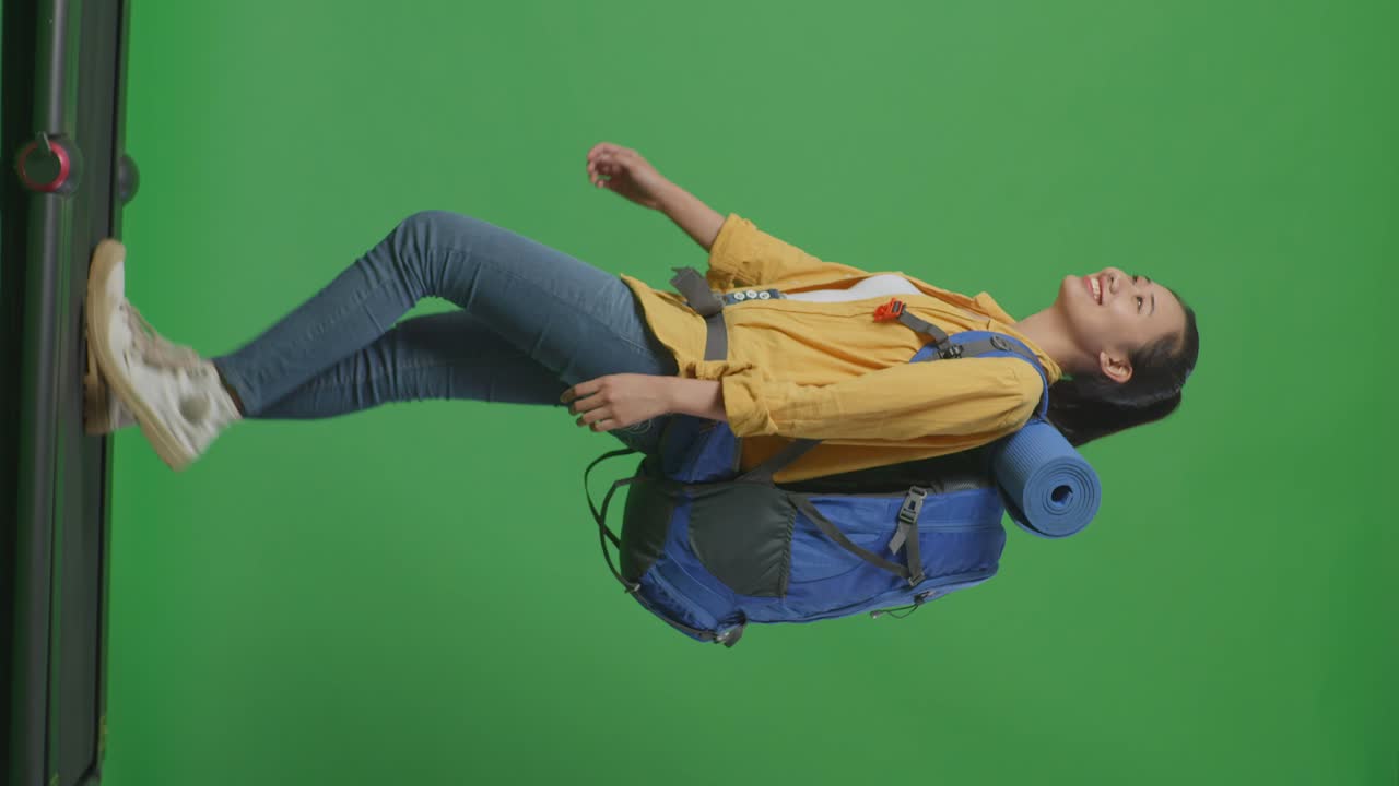 vista lateral completa del cuerpo de una excursionista asiática con mochila de montañismo mirando a su alrededor mientras camina en una cinta de correr en el fondo de la pantalla verde en el estudio