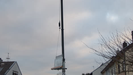 truck crane slowly lifts a frame with windows over a multi-storey residential building