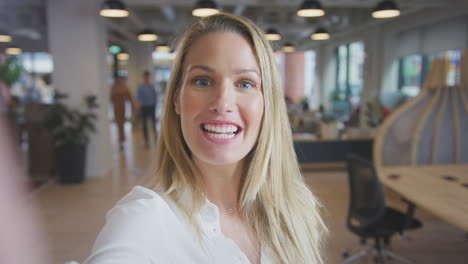 portrait of young businesswoman vlogging into camera in modern open plan office