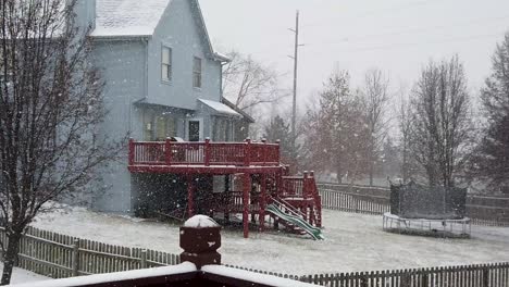 Slow-motion-snow-falling-looking-in-a-backyard-at-a-house-with-a-trampoline