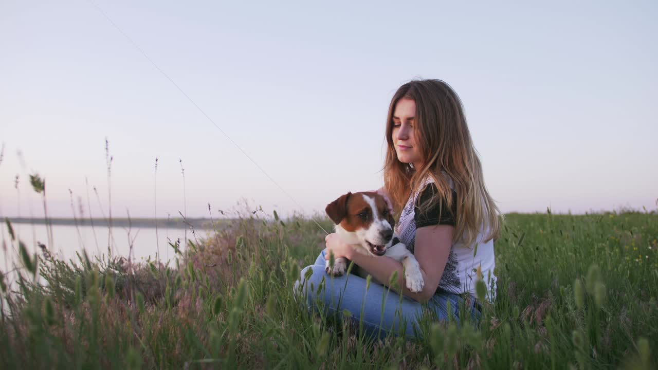행복 한 젊은 여자 와 작은 개 는 해 가 지는 동안 광야 에 날아다니는 날개 와 함께 앉아 있다
