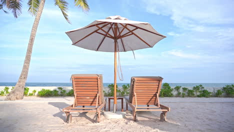 a pair of empty beach loungers under a shade umbrella point out to an ocean view