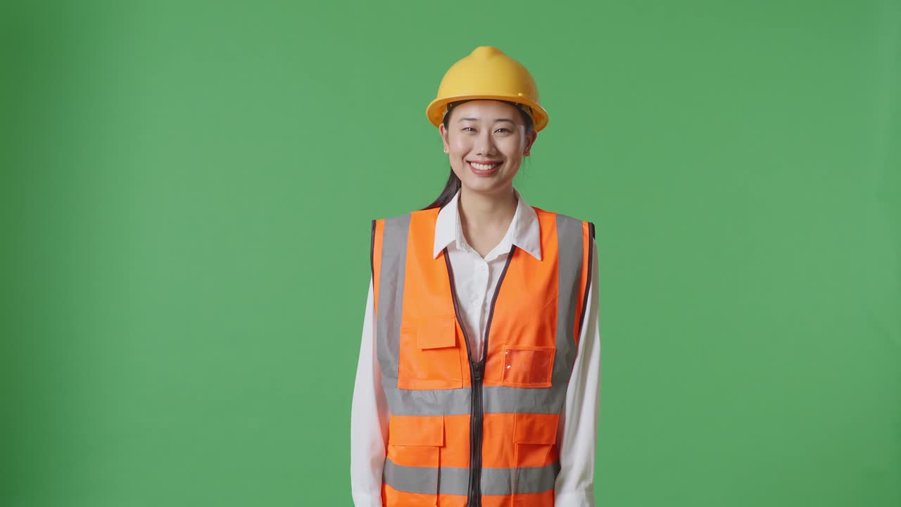 Asian Female Engineer With Safety Helmet Smiling To Camera While Standing In The Green Screen Background Studio