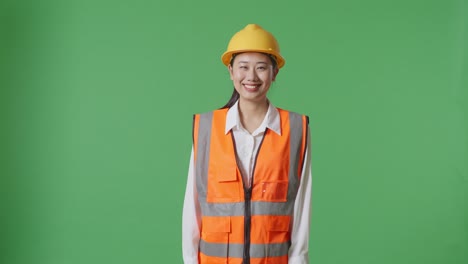 asian female engineer with safety helmet smiling to camera while standing in the green screen background studio