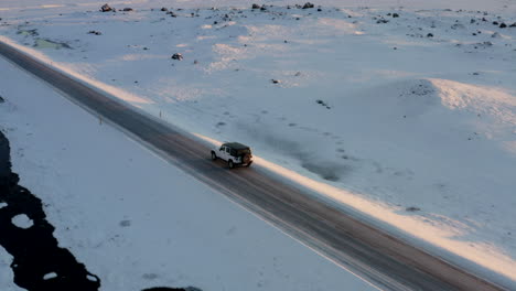 AERIAL:-Flying-besides-Jeep-on-snowy-road-in-Iceland-at-Sunset-Winter,-Sun,-Arctic