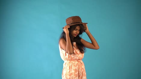 Una-Joven-India-Vestida-De-Naranja-Con-Un-Sombrero-Y-Parada-En-Un-Fondo-Azul-Aislado