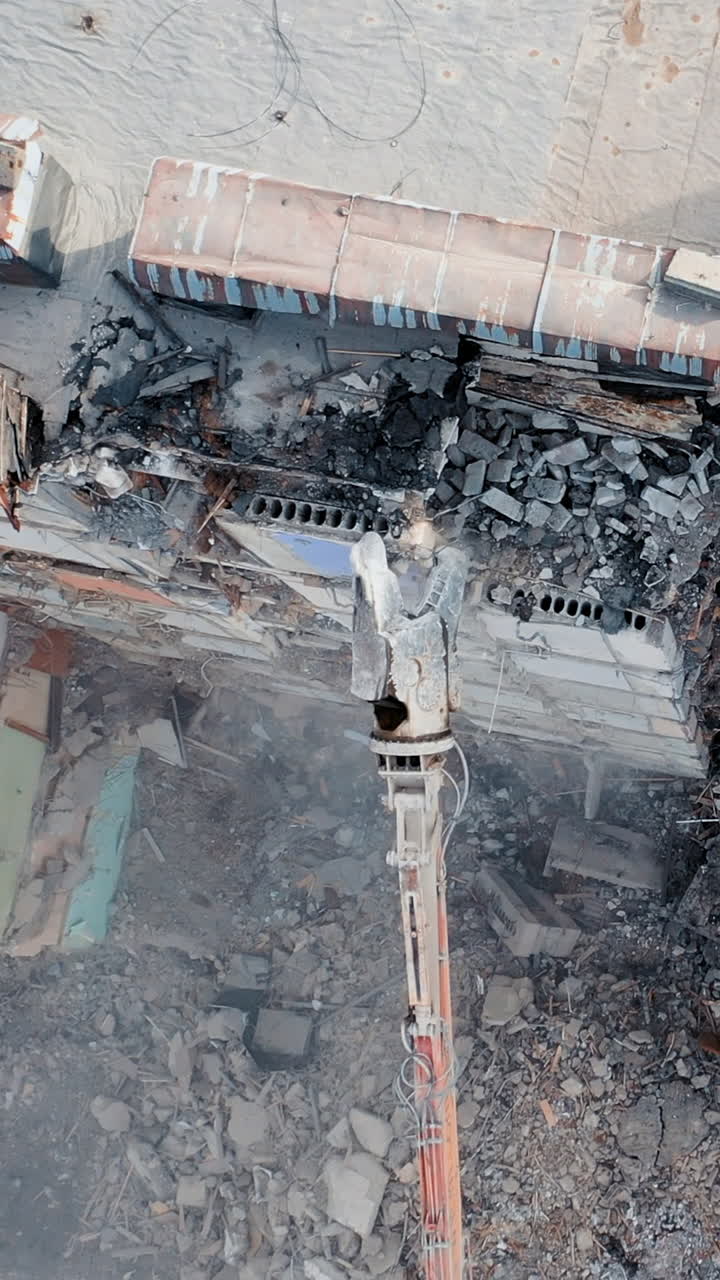 Clearing damage on a construction site using special equipment for a tractor. Demolition of a multi-storey building. Construction garbage. Vertical video
