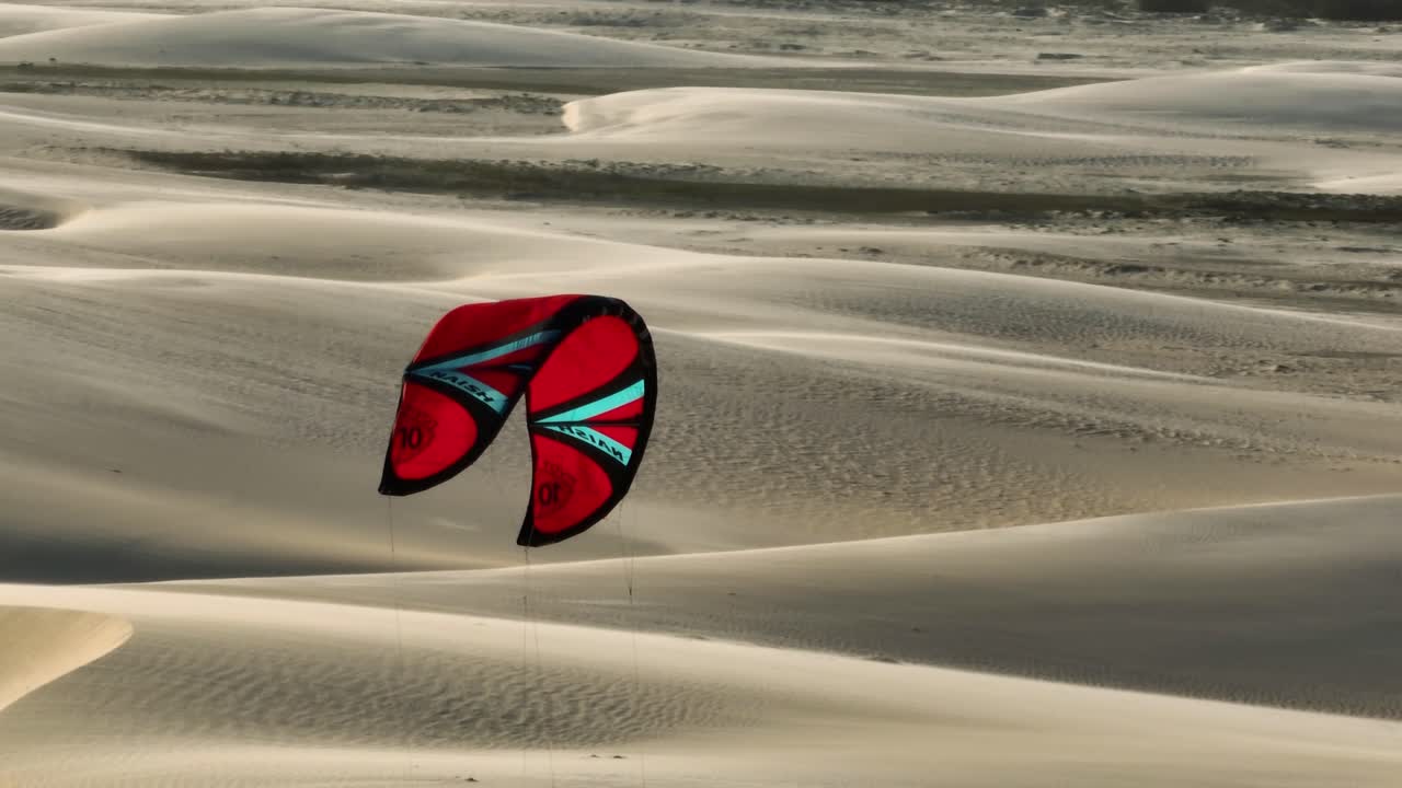 화창한 날 브라질의 모래사막을 따라 날아가는 붉은색 연 - 공중 추적 샷