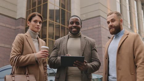 bottom view of caucasian businesswoman holding coffee, african american man watching to a tablet and caucasian man in the street in autumn