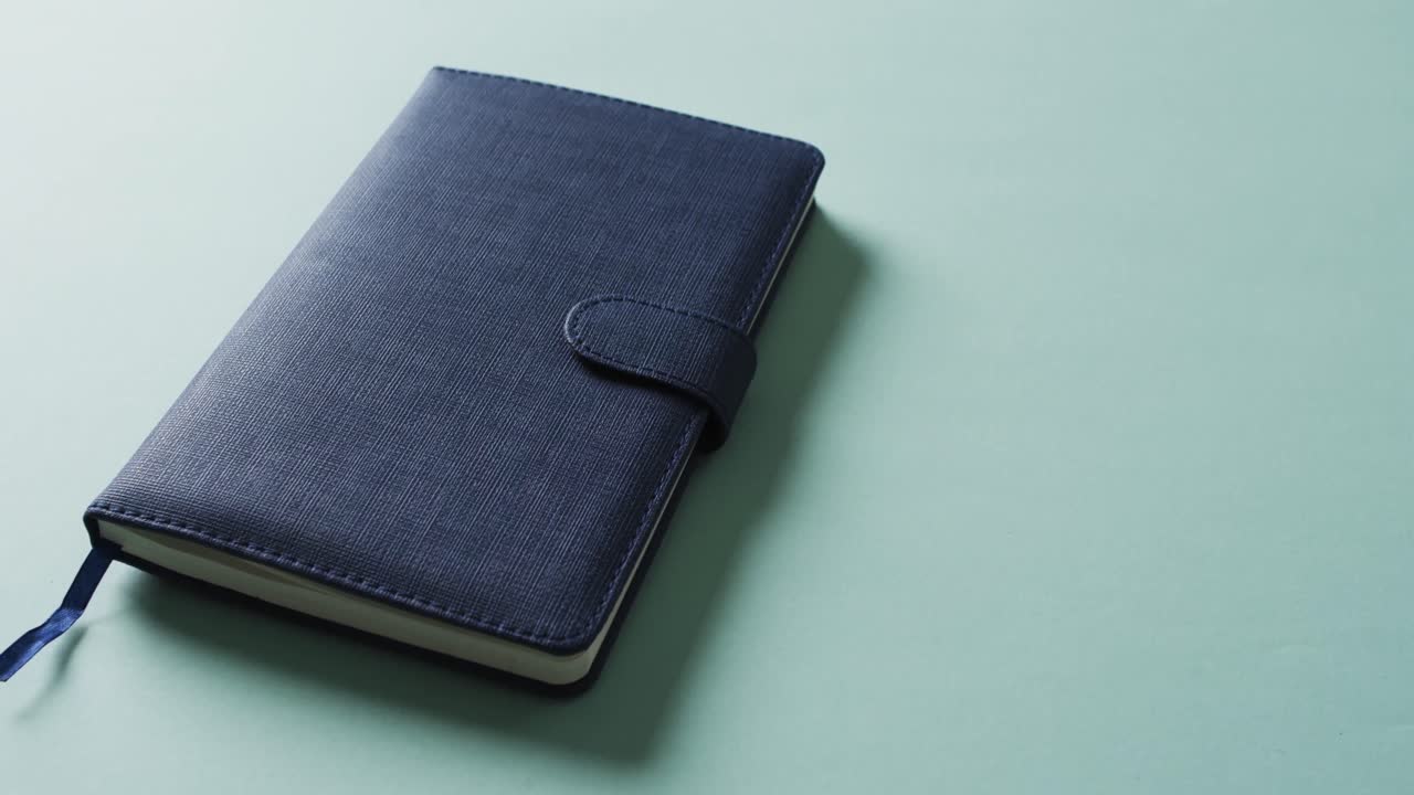 Close up of closed blue notebook with copy space on green background in slow motion