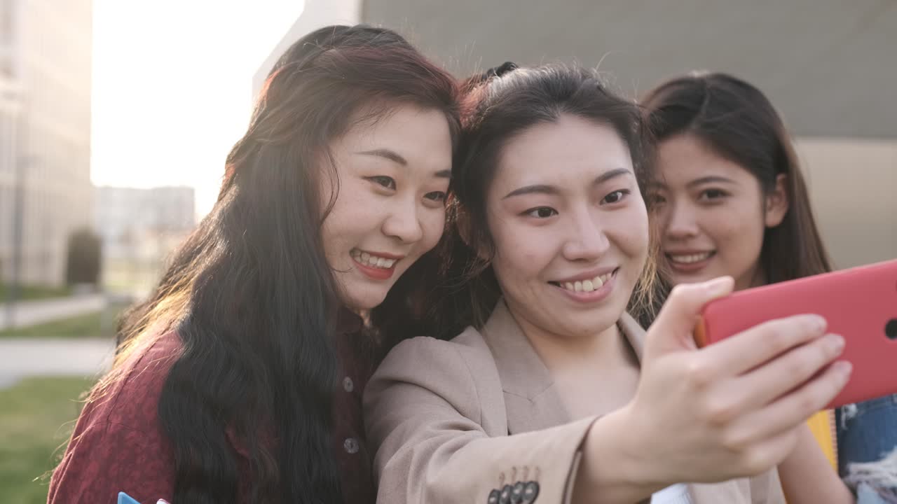 Asian college students taking a selfie with a mobile phone while standing outside the university campus. Education concept.
