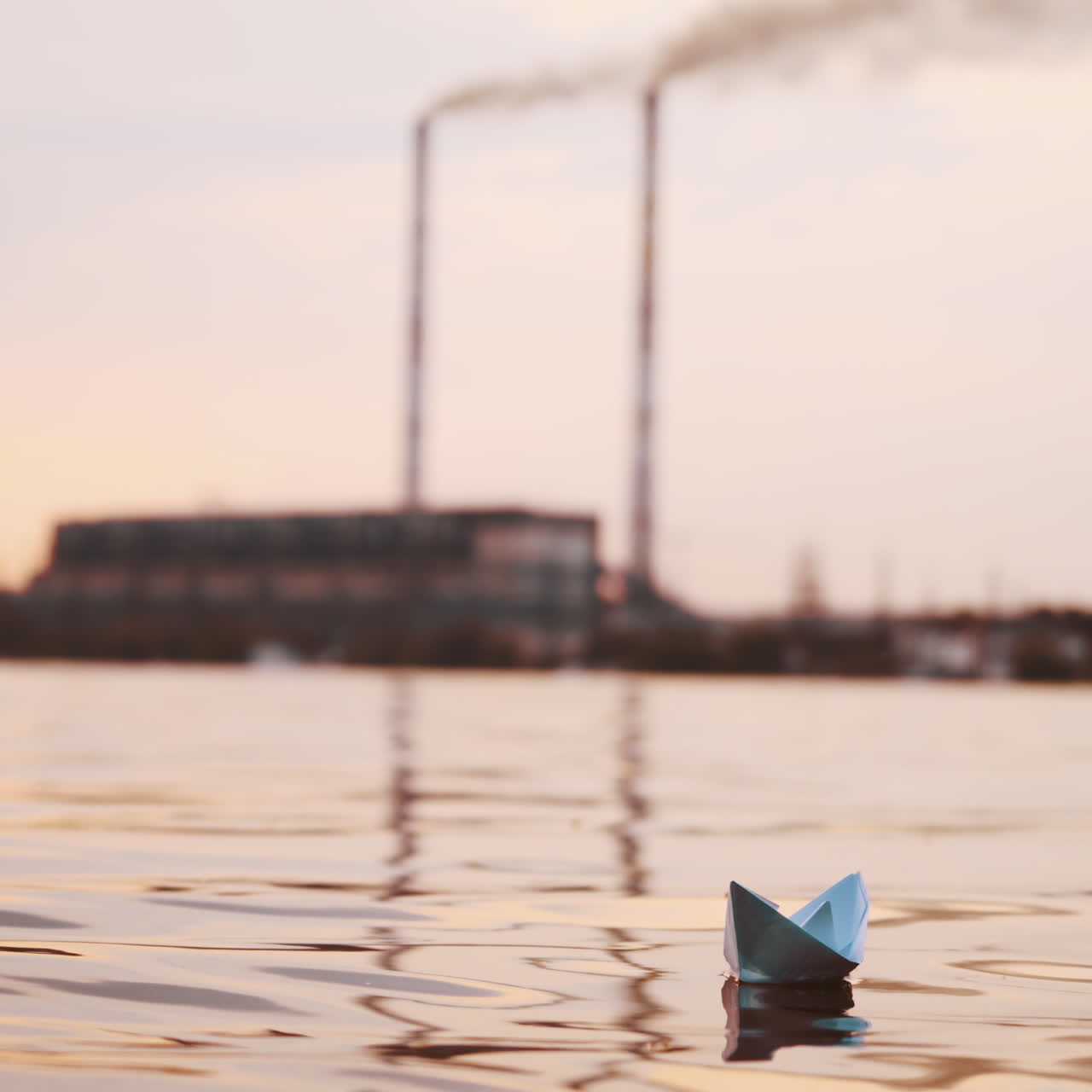 One paper boat in the river on blur factory background. Origami boat sailing in the evening water outdoors.