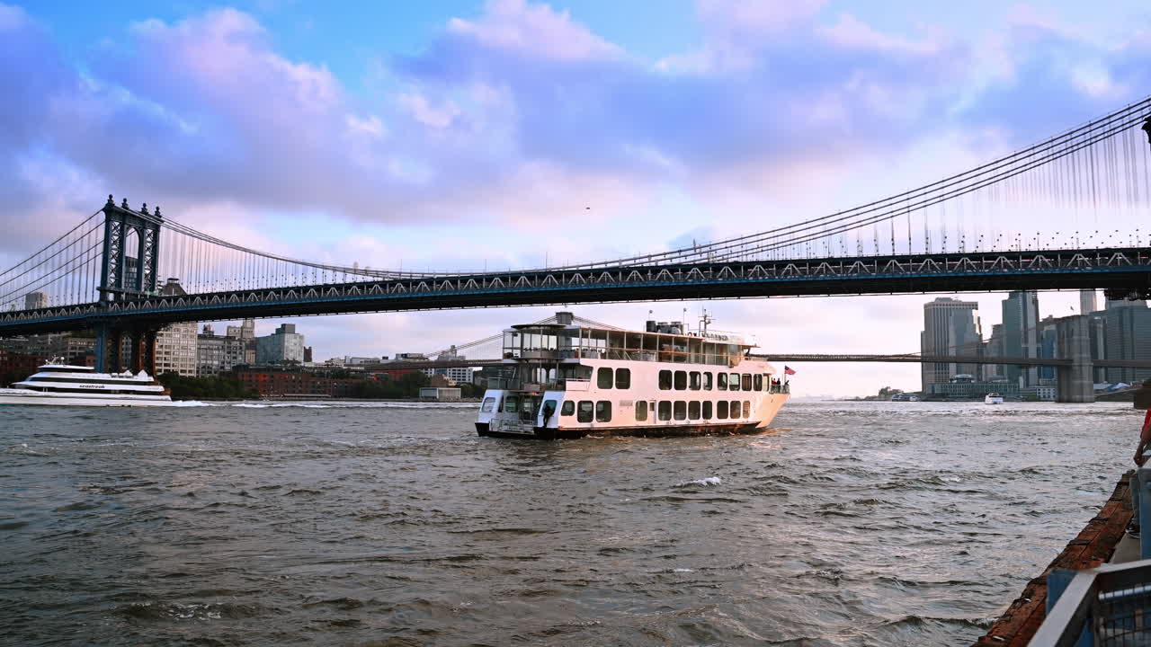 Passagerfærge sejler under Manhattan Bridge i New York City. En hvid passagerfærge krydser East River under Manhattan Bridge med byens skyline i baggrunden