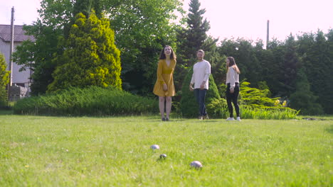 distant view of two caucasian young women and a man playing petanque in the park on a sunny day