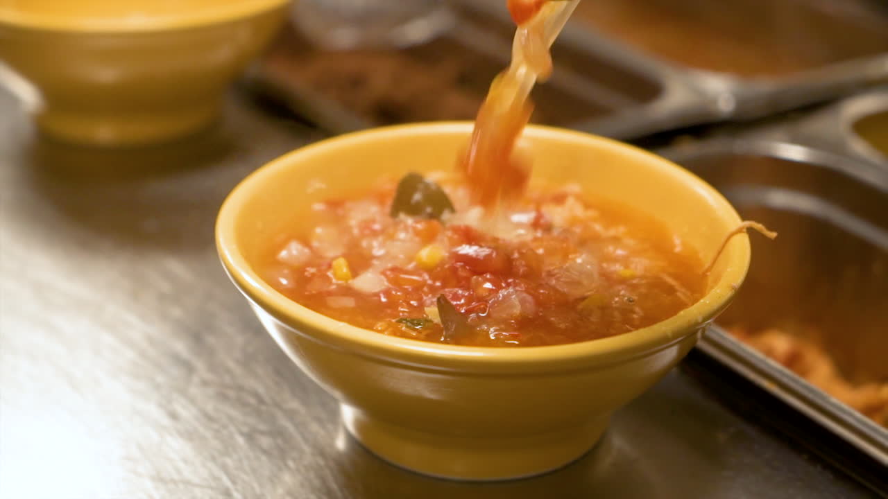 Cook ladles soup and pours into yellow bowl, filling a warm cozy bowl of caldo soup, slow motion close up HD