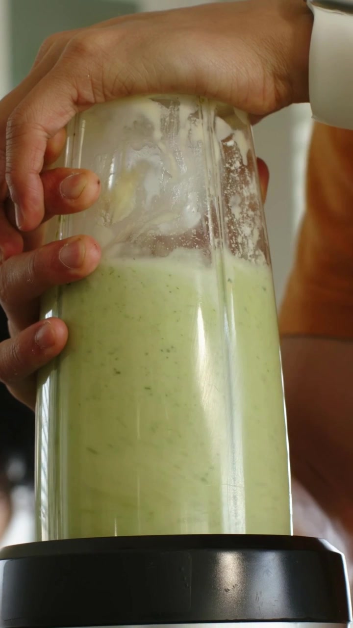 Video verticale: Tenendo una tazza con un mix verde a casa, indossando un top arancione che stabilizza mentre il frullatore è in funzione