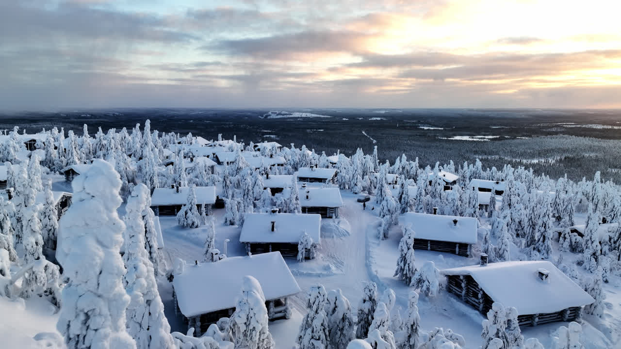 눈 인 나무 위 를 날아다니며, 산 꼭대기 에 있는 오두막 마을 을 향해, 라플랜드 의 겨울 해가 지는 모습 - 공중 에서 볼 수 있는 모습