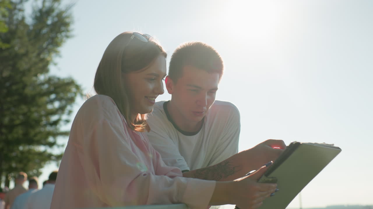 друзья смеются и разговаривают на открытом воздухе с очками на голове женщины, солнце создает теплое свечение, люди ходят на заднем плане, окружены зелени