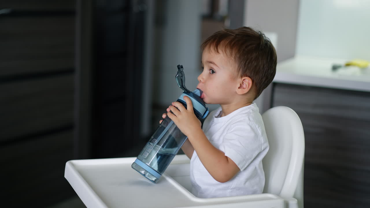 Adorable baby boy drinking water from sport bottle. Kid closes a bottle and looks attentively at camera.