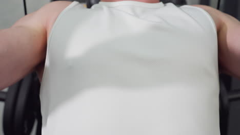 close up of male trainer chest in white singlet straining under tension on chest press machine muscles flexing sweat glistening shirt pushing handles up and down with power cardio