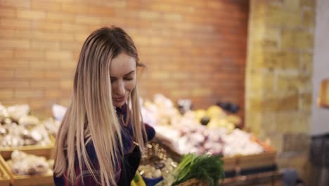 smiling worker in black apron arranging greens in supermarket, having fun during work