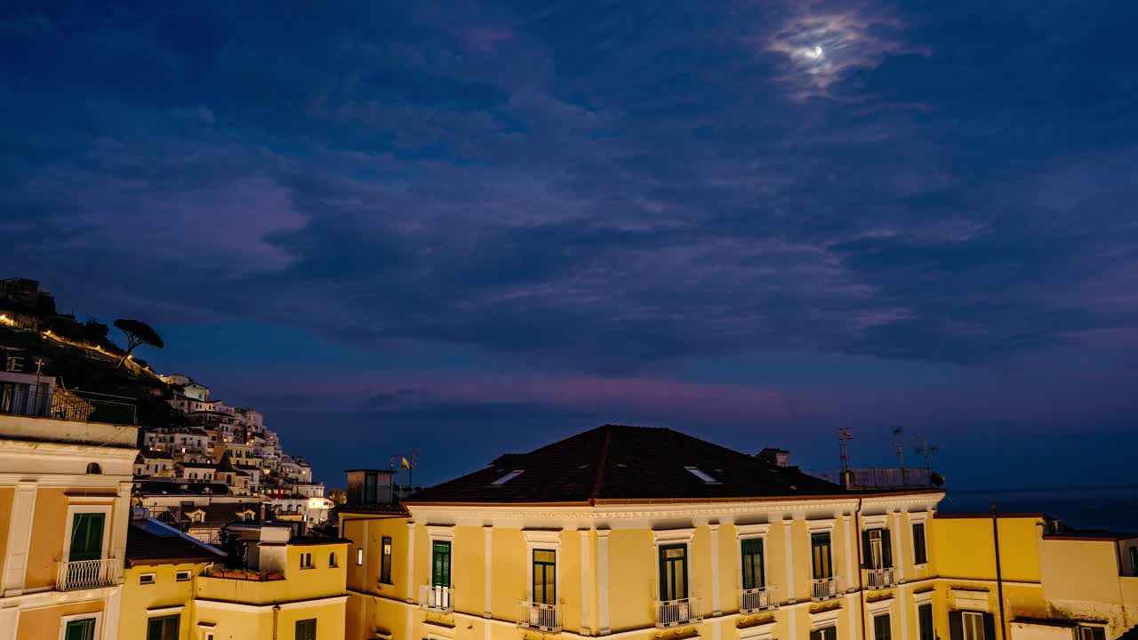 Timelapse vibrante del crepuscolo attraverso gli edifici della città di Amalfi, tetti in terracotta e orizzonte costiero sotto un cielo colorato, serena atmosfera mediterranea nell'Italia meridionale. Centro storico di Amalfi.