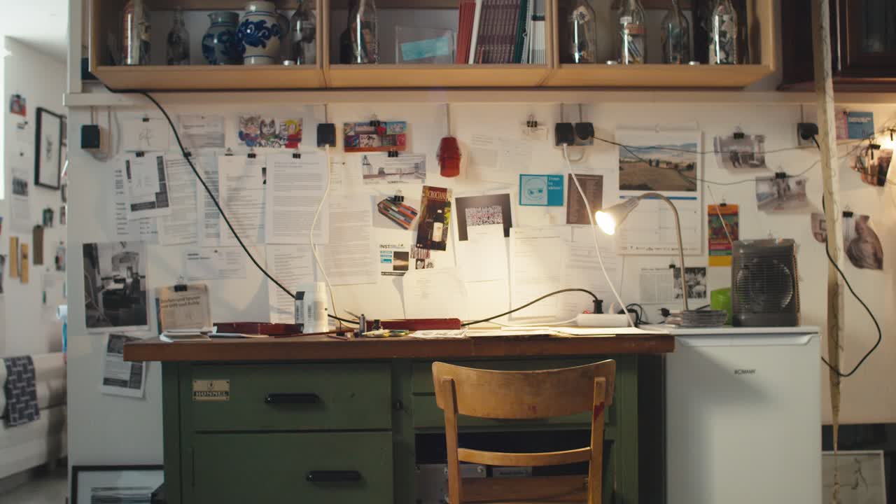 escritorio de artista verde con un montón de papeles en la pared, caos creativo, cámara empujar en