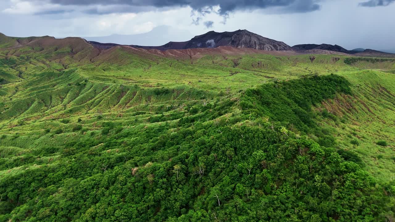 Rising aerial shot over lush mountain greenery in the Philippines, tilting up to reveal Taal Volcano in the distance, showcasing the beauty of this tropical landscape.
