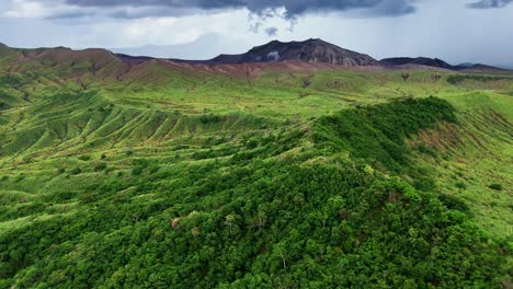 rising aerial shot over lush mountain greenery in the philippines, tilting up to reveal taal volcano in the distance, showcasing the beauty of this tropical landscape.