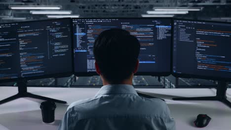 back view of asian man developer using computer to write code with multiple screens in data center