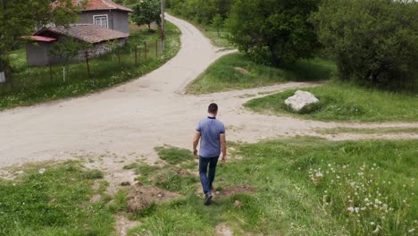 Approaching-drone-shot-on-a-tourist-walking-towards-a-rock-landmark-in-the-middle-of-a-road-in-the-village-of-Tsarichina-Hole-in-Bulgaria