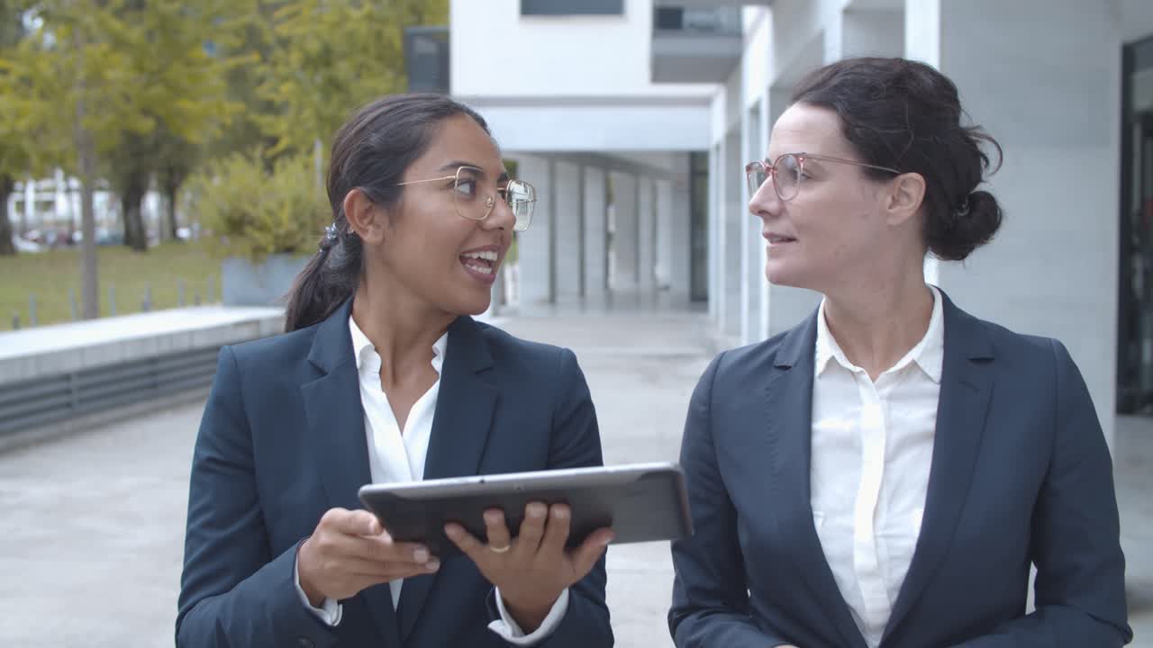 Front view of female managers discussing project on tablet while walking at office building