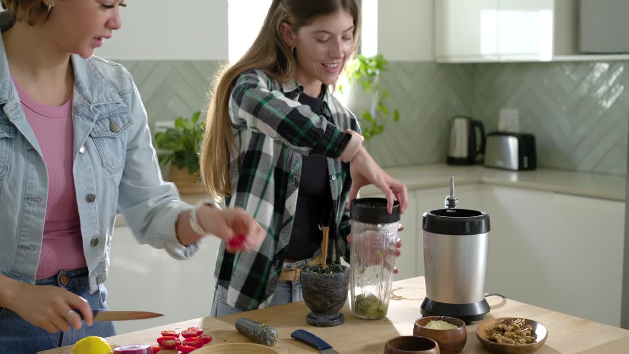 Diverse amiche posizionano un barattolo, affettano ravanelli, pestano erbe in un mortaio e mescolano una salsa sul bancone.