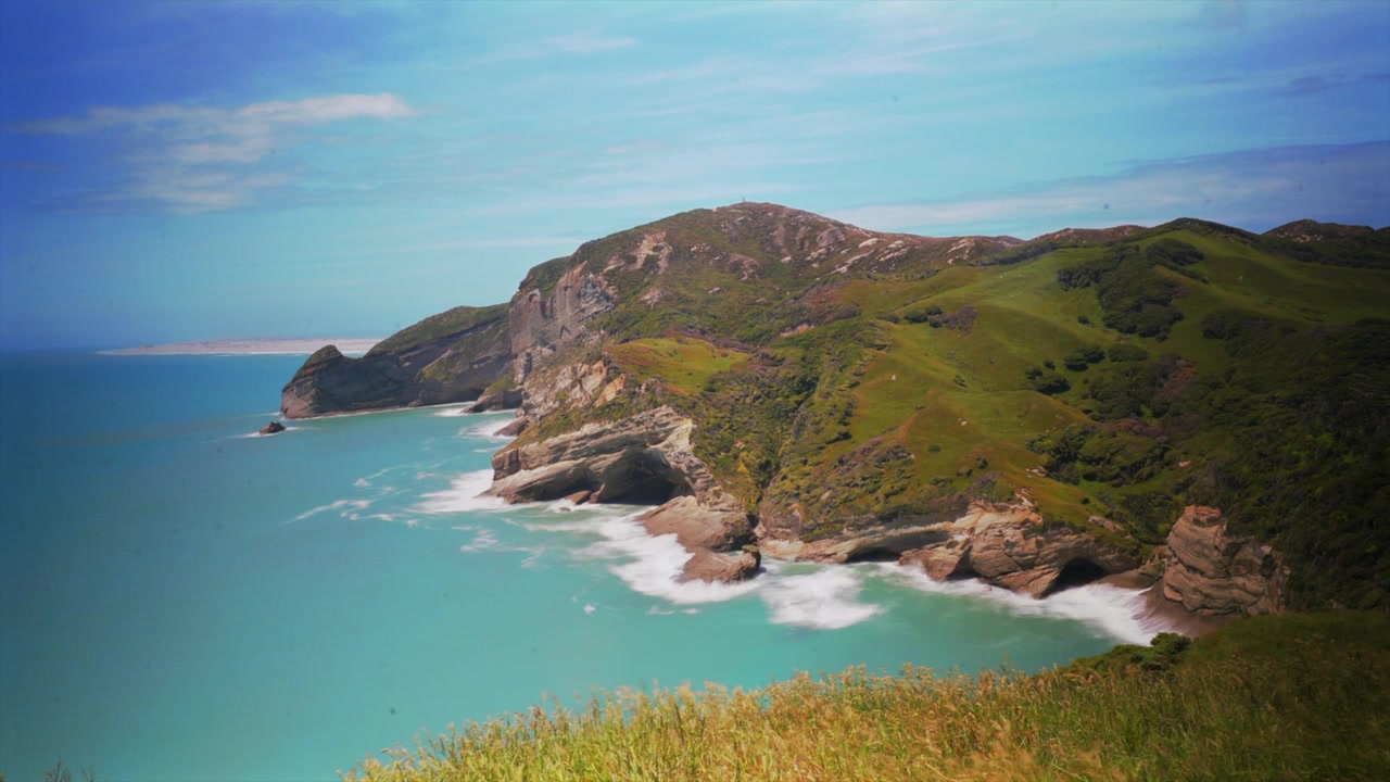 Time-lapse della passeggiata in collina di Cape Farewell, terreni agricoli dell'Isola del Sud, Nuova Zelanda. Puponga Farm Park, Wharariki Beach, Regione di Tasman, Oceano Pacifico meridionale. Paesaggio costiero frastagliato con cielo blu soleggiato di giorno.