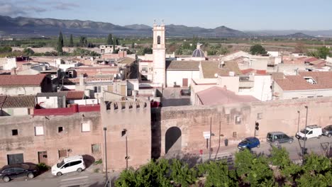 Slow-high-angle-fly-by-over-the-medieval-walled-Village-of-Mascarell-and-its-rooftops-and-bell-tower-in-Spain