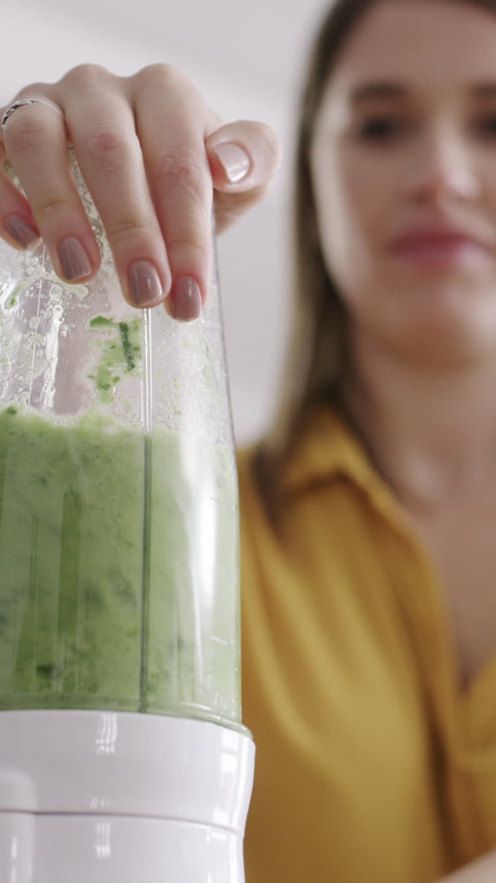 Primo piano di una donna che frulla un frullato verde in cucina