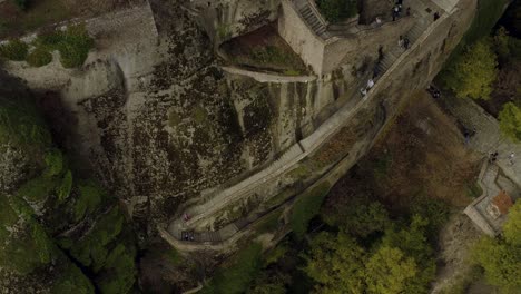 Aerial-view-of-tourists-walking-steep-stairs-to-up-to-a-monastery,-in-Meteora,-Greece---tilt,-drone-shot